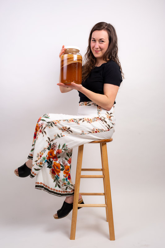 Woman holding kombucha scobys sitting on a chair and smiling 