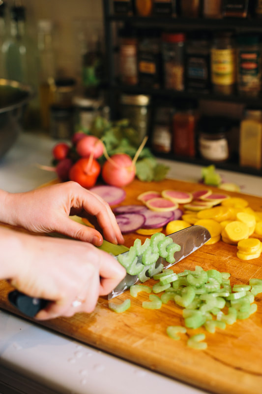 Celery being cut on a cutting board with variety of other sliced vegetables in the background