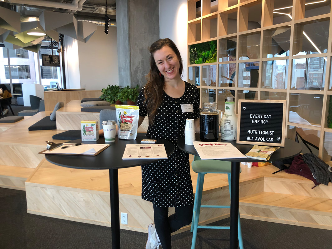 Woman standing behind two tall tables welcoming guests to Everyday Energy class