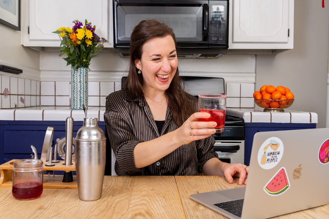 Woman teaching virtual workshop in front of computer holding drink