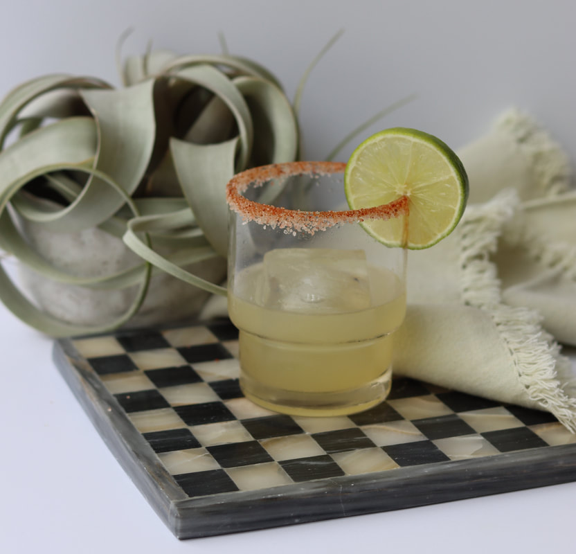 Non-alcoholic margarita mocktail with paprika and salt rim and lime garnish on checkered board with napkin and plant in background