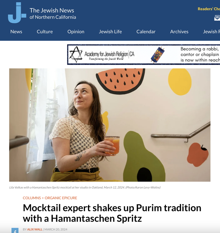 Online article from Jweekly with woman holding mocktail in front of fruit background 
